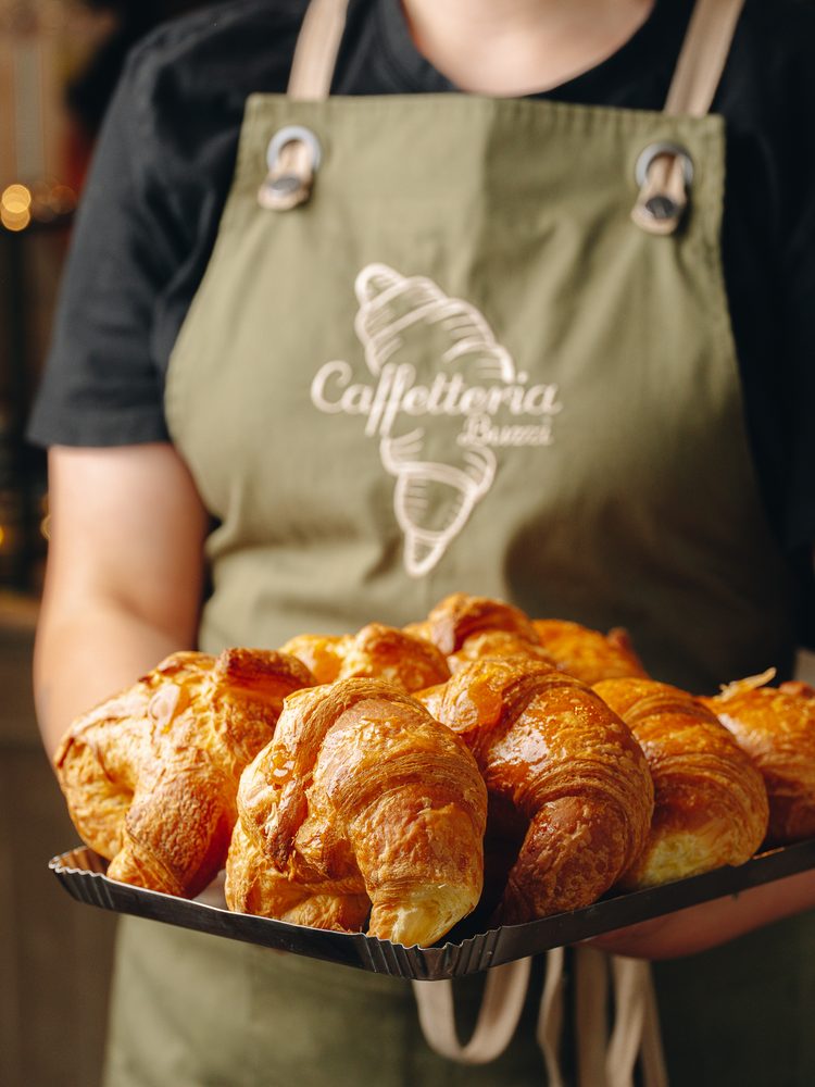 Un vassoio di cornetti appena sfornati, nel grembiule della caffetteria
